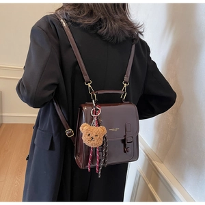 Detail eines dunkelbraunen Rucksacks aus Kunstleder mit Plüschbär-Anhänger und Glanzeffekt