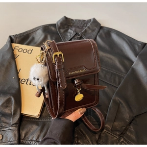 Detail of a chocolate brown oily leather crossbody bag with a fuzzy plush charm