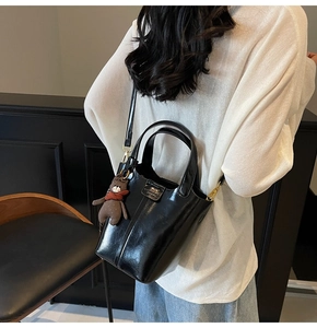 Detailed view of shiny black bucket bag with plush bear charm and golden metal hardware