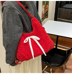 Detail of red plush shoulder bag with a white bow shown on model in a cozy festive setting