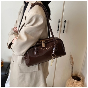 Detail of dark brown leather Boston bag with gold padlock and key charms worn by model