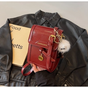 Close-up of burgundy crossbody bag in glossy cracked leather with plush charm