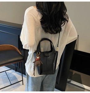 Detailed back view of a black leather bucket bag with a cute brown plush bear charm