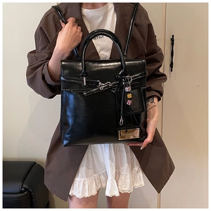 Détail du sac à main noir brillant avec boucle emblématique et breloque en perles chic