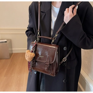 Detail der vintage schokobraunen Ledertasche mit doppelten Schnallen und einem Plüschbär-Anhänger
