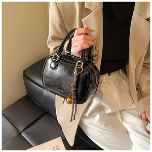 Detail of glossy black patent leather handbag with gold hardware and bell ornament