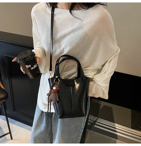 Detail of black glossy bucket bag with cute bear charm and adjustable shoulder strap