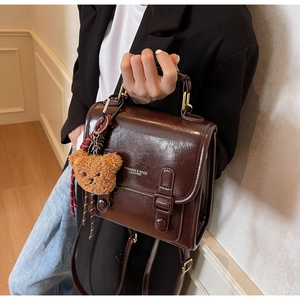 Detail der braunen Retro-Ledertasche mit einem niedlichen Plüschbären-Anhänger an der Seite