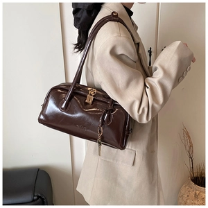 Detail of vintage dark brown shoulder bag with gold padlock and key charm on beige blazer
