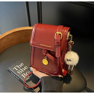 Detail of burgundy crossbody phone bag featuring gold lettering and a plush keychain charm
