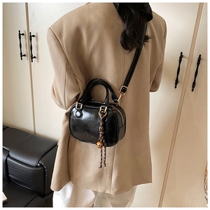 Detail of black glossy mini square bag with gold hardware and tassel charm on model