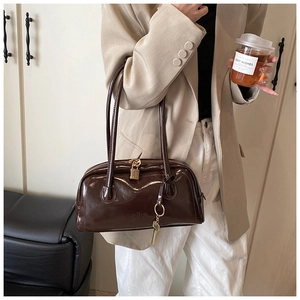 Detail of a dark brown glossy commute bag with gold lock and key pendant on a model