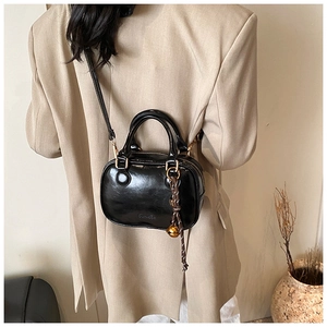 Detail of a black glossy crossbody bag with a brown cord and gold bell charm accessory
