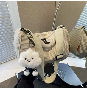 Detail der cremeweißen Cord-Zylindertasche mit Plüschwolken-Anhänger und breitem Gurt