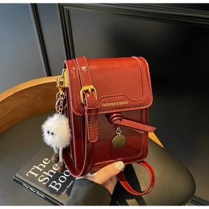 Detail of red patent leather phone bag with gold buckle and fuzzy monster charm