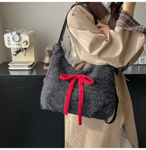Close-up of dark grey tweed shoulder bag featuring a vibrant red plush bow detail