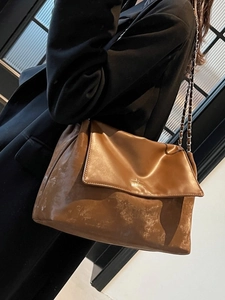 Vintage brown leather tote bag with chain strap worn by a model in a black suit
