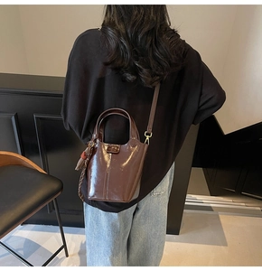 Brown patent leather bucket bag featuring a decorative silk scarf and slender strap