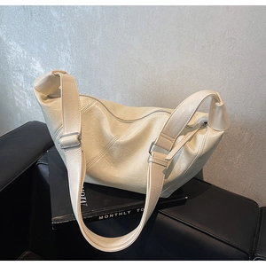 Detail of a minimalist cream white soft leather crossbody bag on a black leather chair