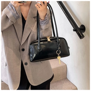 Detail shot of glossy black patent leather shoulder bag with golden key charm and lock