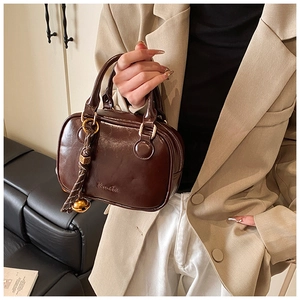 Detail of a dark brown glossy leather handbag with decorative metal ball charm