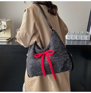 Detail shot of plush grey shoulder bag with a large red bow in a cozy home setting