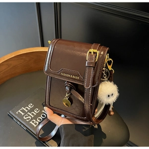 Detail of dark brown leather crossbody bag with gold hardware and plush charm