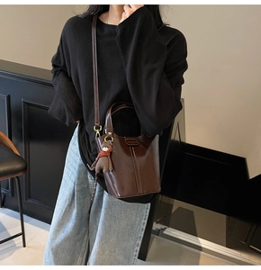 Brown patent leather bucket bag with cute bear charm worn by a model in casual style