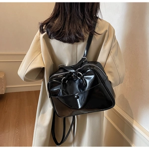 Detailed view of the shiny black leather shoulder bag with metallic zippers on a model