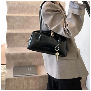 Detail of glossy black patent leather shoulder bag with gold hardware on a gray blazer