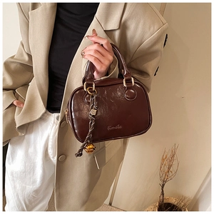 Detail of a brown leather Boston bag featuring gold hardware and a woven bell pendant