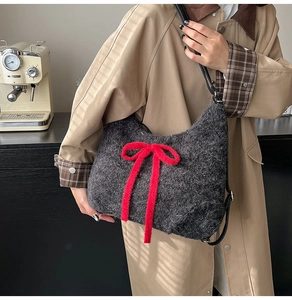 Detail of dark grey plush hobo bag featuring a large red bow and slim leather strap