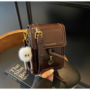 Detail of dark brown polished leather phone bag with gold lettering and plush monster charm