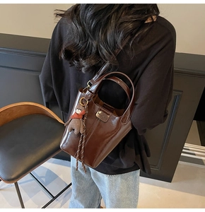 Detail of dark brown polished bucket bag with a cute bear charm and metallic hardware