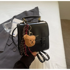 Detail eines schwarzen Lederrucksacks mit Klappe, Tragegriff und niedlichem Bärenanhänger