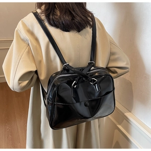 Model wearing a black glossy leather backpack with silver zippers and a minimalist design