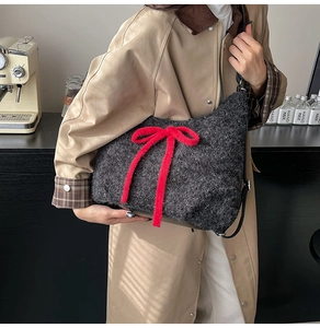 Detail of dark grey plush tote bag featuring a large red bow and leather strap