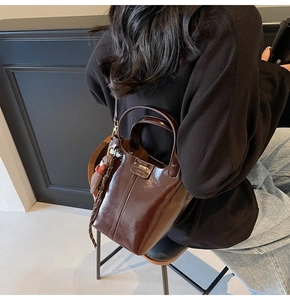 Close-up of a dark brown glossy bucket bag with a plush bear charm and metallic handles