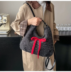 Detail of grey plush tote bag with a red ribbon bow worn by a model in a cafe