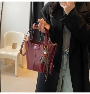 Detail of burgundy glossy leather bucket bag with cute bear charm held by model