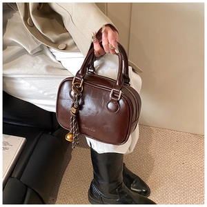 Detailed view of dark brown high-gloss handbag with gold zipper and charms