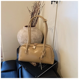 Detail of beige bowling bag featuring golden lock charm and embossed logo on glossy leather