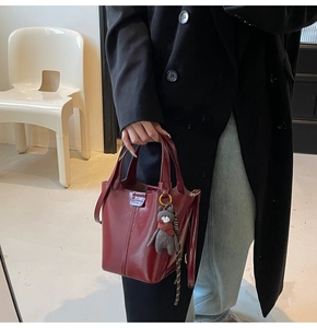 Detail of burgundy glossy bucket bag with metal logo and cute bear charm pendant