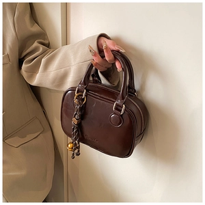 Close-up of a dark brown leather square bag with golden hardware and braided pendant