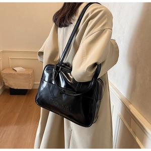 Close-up of black glossy leather tote bag showing fine texture and shoulder strap detail