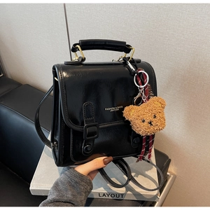 Detailaufnahme der schwarzen glänzenden PU-Handtasche mit Tragegriff und Bärenanhänger