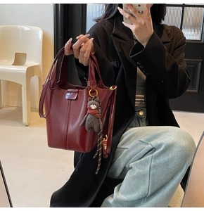 Detail of burgundy bucket bag with glossy leather texture and small bear charm