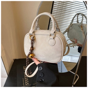 Detail view of grey crossbody bag featuring golden hardware and braided rope charm