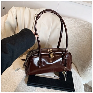 Detail of dark brown glossy leather handbag with gold lock and branded embossed logo