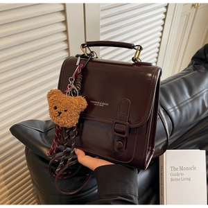 Detail der dunkelbraunen Lederhandtasche mit Klappverschluss und Plüschbär-Anhänger